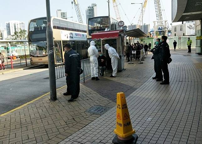 該男子坐在巴士站旁，幾名身穿防護衣的人員圍着他了解事件。