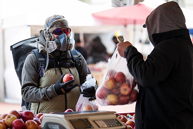 A customer wearing a protective face mask and gloves, left, buys apples at a farmers market in San Francisco on Wednesday. Photo: Bloomberg