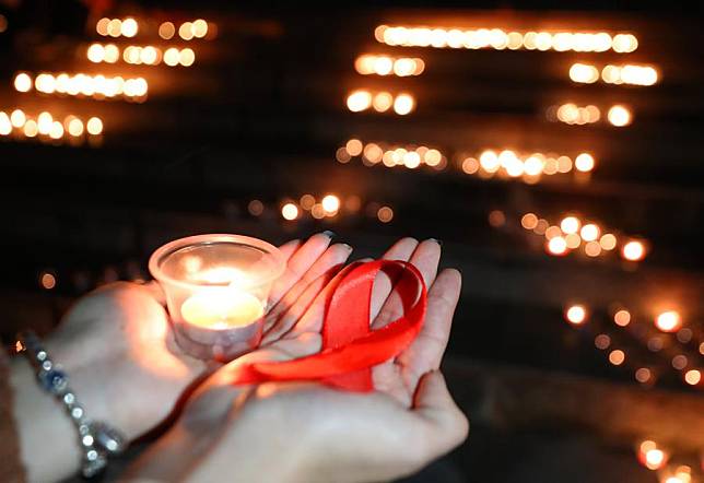 People hold a candle and a red ribbon during an event to raise awareness of AIDS at University of South China in Hengyang, central China's Hunan Province, Nov. 29, 2023. (Photo by Cao Zhengping/Xinhua)