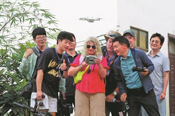 Photographers and designers gather around Joerdis Montgomery, a filmmaker from Berlin, Germany, as she operates a drone to capture aerial shots of a village in Libo county, Guizhou province, on Sept 12, 2024, during a five-day trip of 31 visual artists in Guizhou. KUANG LINHUA/CHINA DAILY