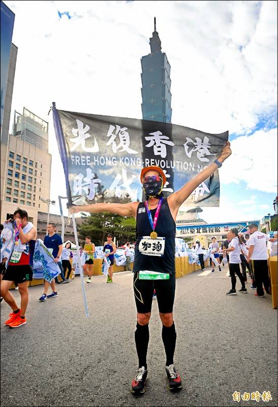 來自香港的跑者，身穿黑色跑衣，並舉著「光復香港，時代革命」的旗幟邁入終點，期盼藉由台北馬，向國際社會傳遞「護民主，挺自由」的訴求。(記者方賓照攝)