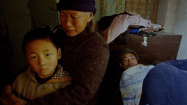 A Chinese AIDS sufferer lies in bed as his mother comforts his young son inside their house in a village in Henan in November 2003.