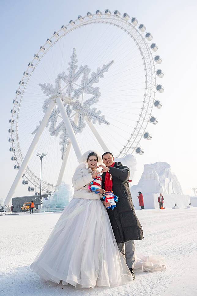 A loving couple pose for photos in front of a snowflake-shaped ferris wheel at the Harbin Ice-Snow World in Harbin, northeast China's Heilongjiang Province, Jan. 6, 2025. (Xinhua/Xie Jianfei)