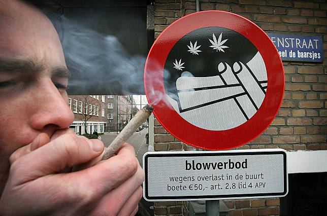 一名男子站在阿姆斯特丹一個寫有「禁止抽大麻」的牌子前抽大麻菸。（點擊右側看更多） 路透社 / 達志影像