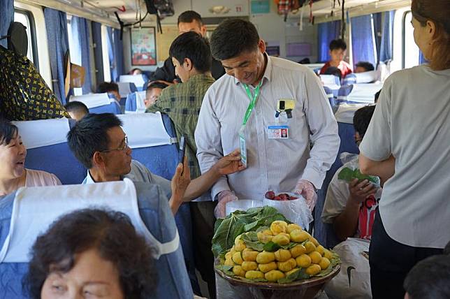 A tourist scans the payment QR code to pay for the figs he bought from vendor Yimamamat Saipar onboard the train No. 7557, Aug. 1, 2024. (Xinhua/Jin Bowen)