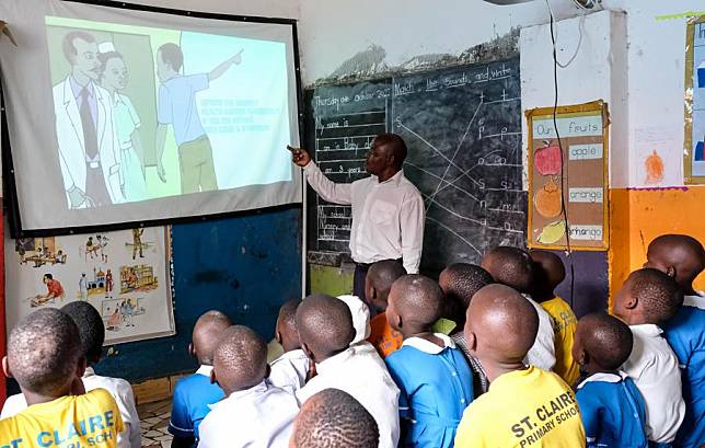 Pupils attend class about Ebola using a StarTimes projector at St. Claire Primary School in Kampala, Uganda, Oct. 13, 2022. The “Access to Satellite TV for 10,000 African Villages” project in Uganda is implemented by Chinese satellite television, StarTimes. (Photo by Hajarah Nalwadda/Xinhua)