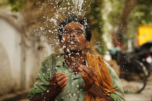 6月13日，印度北方邦安拉阿巴德，一名勞工往臉上潑水降溫（美聯社）