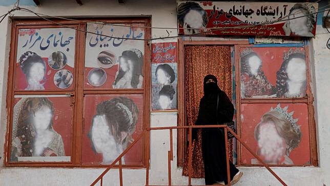 2021年10月6日，阿富汗喀布爾，一名穿罩袍的婦女進入一家美容院，店外海報上的女性臉孔都已被塗掉。路透社