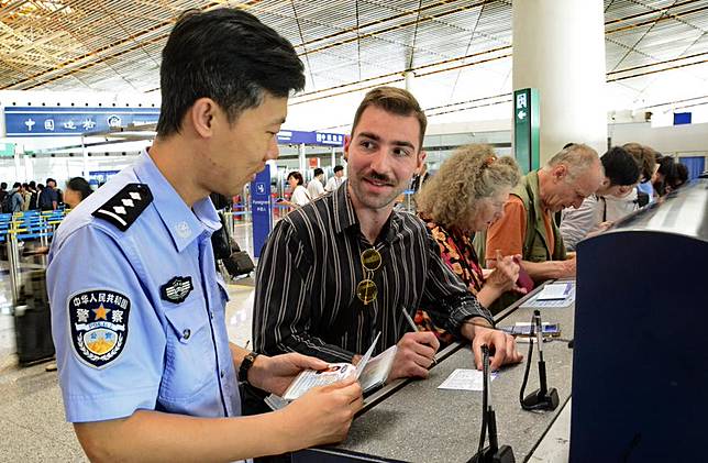 A police officer assists an American tourist fill out an entry registration card at the border check section of Beijing Capital International Airport in Beijing, capital of China, July 10, 2024. (Xinhua/Li Xin)