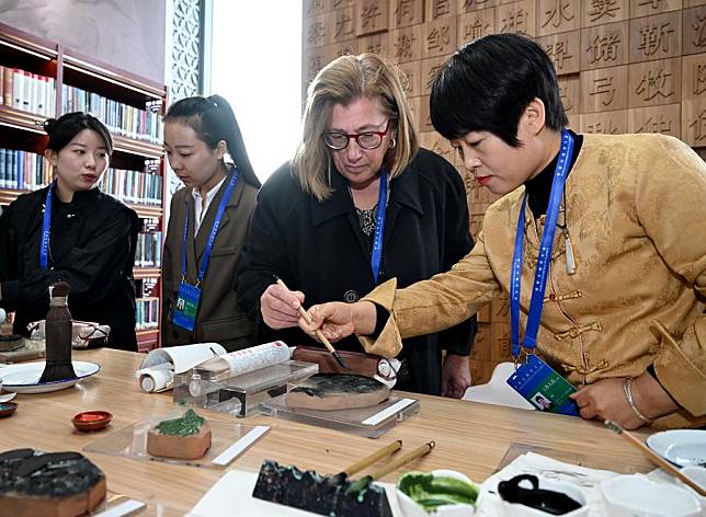 A foreign visitor (2nd R) experiences woodblock printing during an exhibition on classical studies achievements in Beijing, capital of China, on Nov. 7, 2024. (Xinhua/Li He)