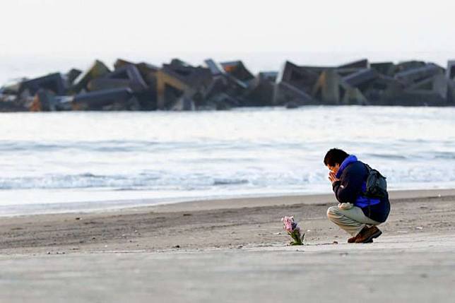 一位日本民眾在311東日本大地震七周年之際，在仙台市的荒濱海灘獨自插了一束花在沙地上悼念亡者。（資料照，美聯社）