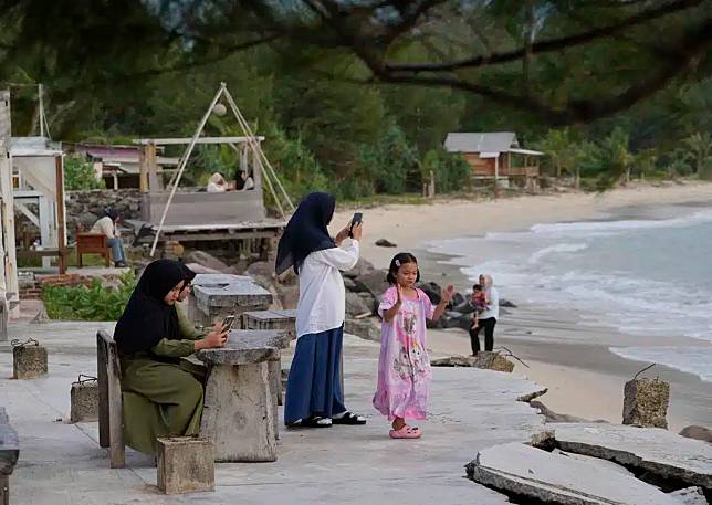 เด็กหญิงใช้โทรศัพท์มือถือขณะเยี่ยมชมหาดลัมปุก หนึ่งในพื้นที่ที่ได้รับผลกระทบหนักที่สุดจากสึนามิในมหาสมุทรอินเดียเมื่อปี 2547 บริเวณชานเมืองบันดาอาเจะห์ ประเทศอินโดนีเซีย เมื่อวันศุกร์ที่ 13 ธันวาคม 2567 (ภาพถ่ายโดย AP Photo/Achmad Ibrahim)