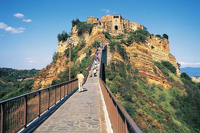 Tourists walk up the single metal footbridge from the main road below to the village of Civita di Bagnoregio in the Latium region near Rome, Italy. The village is perched on a plateau of volcanic rock surrounded by steep ravines and is home to just a dozen residents. Photo: DeAgostini/Getty Images