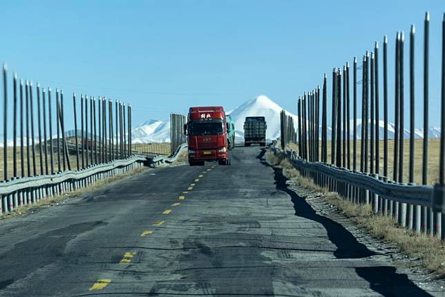 Trucks pass through a road section of the Qinghai-Xizang Highway built on permafrost flanked by metal pipes, which serve as conductive heat pipes to stabilize the temperature of the permafrost layer, on the Qinghai-Xizang Plateau in northwest China's Qinghai Province, Dec. 2, 2024. (Xinhua/Jiang Fan)