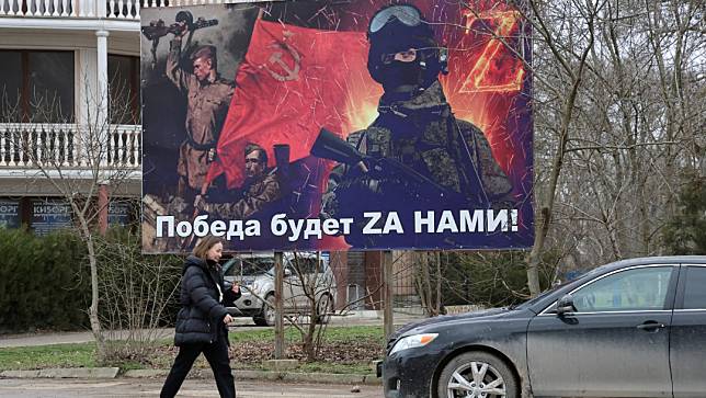 2024年1月25日，克里米亞黑海村（Chernomorskoye）一名婦女走過俄國政府募兵宣傳看板。路透社