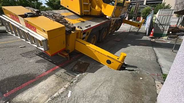 大型吊車車體失衡傾斜，後方油壓支撐腳將人行道壓出一個大洞。民眾提供