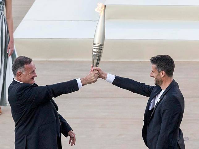 Hellenic Olympic Committee president and International Olympic Committee (IOC) member Spyros Capralos (L) passes the flame to Tony Estanguet, president of the Paris 2024 organizing committee during the handover ceremony at Panathenaic stadium in Athens, Greece on April 26, 2024. (Xinhua/Marios Lolos)