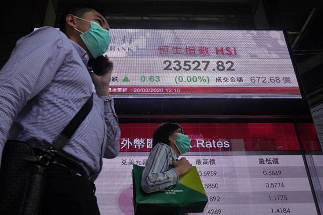 People wearing face masks walk past an electronic board displaying the Hang Seng Index price on March 26, 2020. Photo: AP