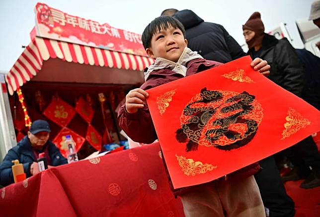 A boy receives a calligraphy work of Chinese character &ldquo;Fu&rdquo;, which means &ldquo;good fortune&rdquo;, at the Poli Market in Qingdao Xihai'an (West Coast) New Area in Qingdao, east China's Shandong Province, Jan. 18, 2025. (Xinhua/Li Ziheng)