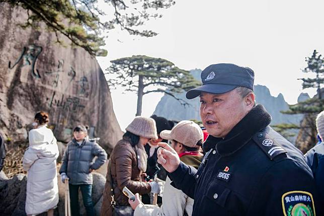 Hu Xiaochun, a staff member responsible for the daily care and observation of the Guest-Greeting Pine, an iconic landmark of Huangshan Mountain, introduces the pine and cliff inscriptions on the mountain to tourists in Huangshan Scenic Area, east China's Anhui Province, Dec. 18, 2024.(Xinhua/Fu Tian)