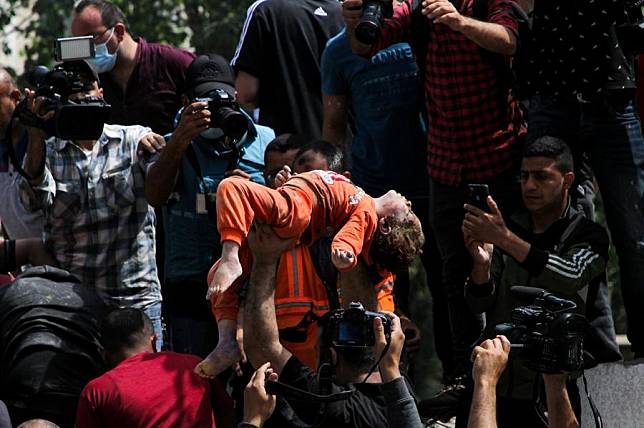 A Palestinian man holds a child who was rescued from the rubble of destroyed houses following Israeli air strikes in Al-Wahda Street in the middle of Gaza City, on May 16, 2021. (Photo by Rizek Abdeljawad/Xinhua)