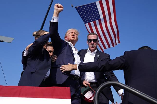 川普在宾州巴特勒市的竞选造势活动遭遇枪击，他离开前高举右手，配上背后飘扬的美国国旗，被认为是「完美构图」。 （美联社）