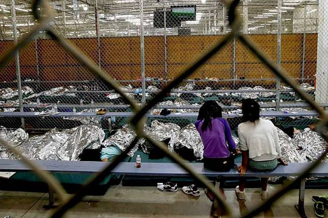 6月18日，美國亞利桑那州一間非法移民兒童安置中心內，兩名女童正在看電視上的世界盃足球賽。這些非法移民兒童被迫與父母分開後，被關在籠子裡（美聯社）