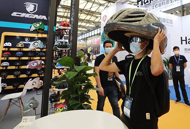 A visitor tries a large model helmet during the 30th China International Bicycle Fair in east China's Shanghai, May 5, 2021. (Xinhua/Fang Zhe)