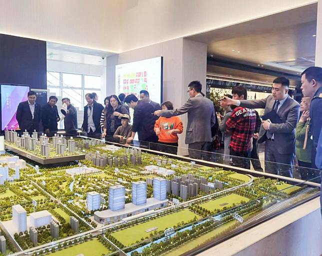 This photo taken with a mobile phone shows people watching a sand table model of a real estate project in east China's Shanghai, May 28, 2024. (Xinhua/Zheng Juntian)