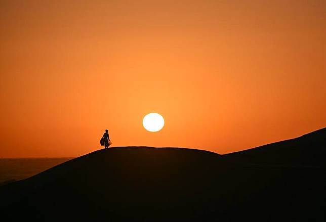 A tourist watches sunrise at the Huludao (Gourd Island) scenic spot in Yuli County, northwest China's Xinjiang Uygur Autonomous Region, Oct. 26, 2024. The unique autumn scenery featuring desert, lakes and the desert poplar (populus euphratica) in the scenic spot attracts many tourists. There are tens of millions of acres of desert poplars scattering in the Tarim River Basin in Xinjiang. (Xinhua/Hu Huhu)