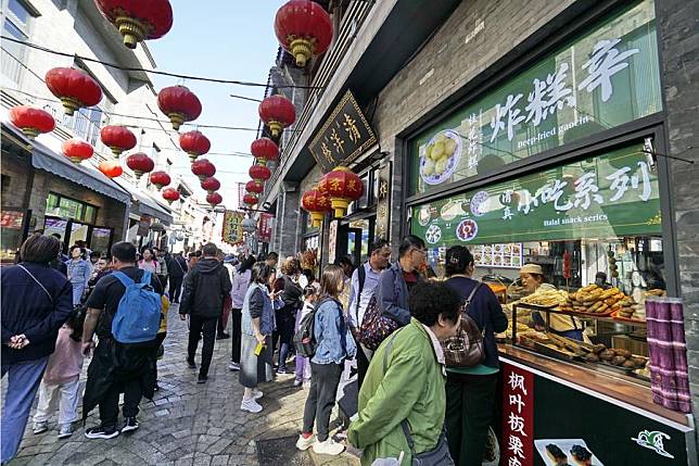 Tourists taste food at the Qianmen pedestrian street in Beijing, capital of China, Oct. 7, 2024. (Xinhua/Li Xin)