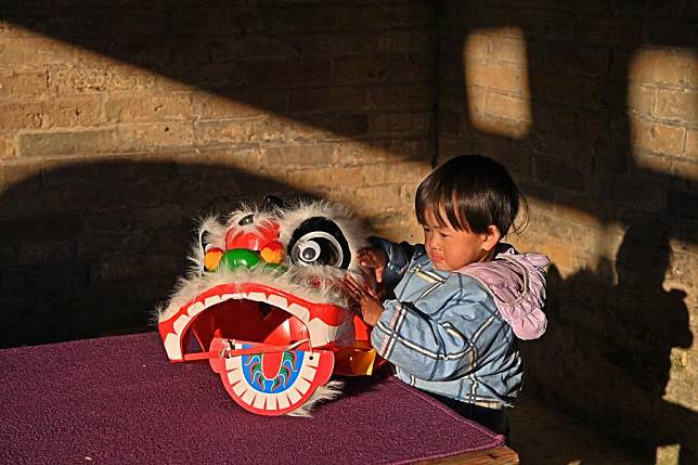 A kid touches the headgear for the lion dance at Longteng Hamlet, Na'an Village in Tongmu Town of Jinxiu Yao Autonomous County, south China's Guangxi Zhuang Autonomous Region, Dec. 19, 2024. (Xinhua/Zhou Hua)