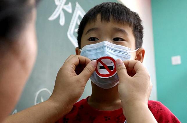 A community worker helps a child to wear a face mask with anti-smoking sign, as the World No Tobacco Day (May 31) draws near, at Shengshiyucheng Community in Shijiazhuang, north China's Hebei Province, May 30, 2020. (Xinhua/Wang Xiao)