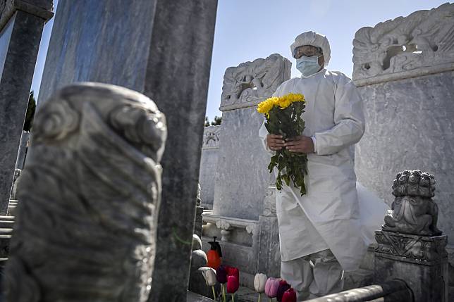 A photo released by Xinhua News Agency shows a cemetery worker in a protective suit makes an offering at a grave site in the Babaoshan cemetery in Beijing on March 28.