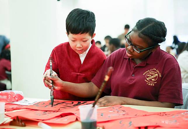 A student from Beijing teaches a student from Medgar Evers College Preparatory School of New York to practice Chinese calligraphy during a culture exchange event in New York, the United States, Feb. 2, 2018. (Xinhua/Wang Ying)