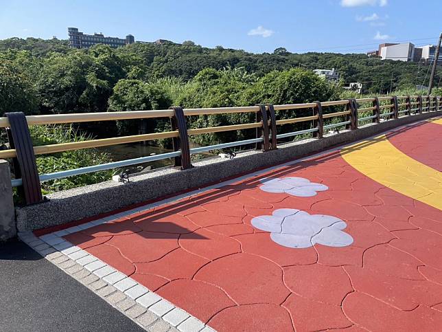 改善後的三芝宋厝橋，橋梁欄杆以不同顏色油漆搭配，增加活潑度；橋面則採用壓印彩色圖樣的瀝青鋪面，平坦又美觀，並設置投射照明燈具，維護原先豐富生態，提升道路安全。（新北市工務局提供）