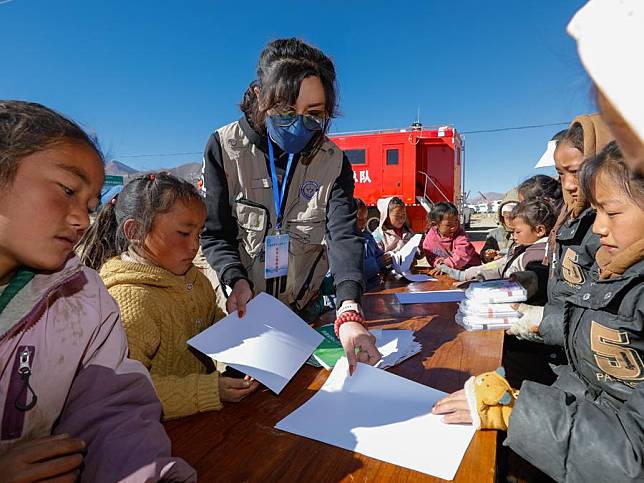 Tan Xiren helps children to paint at a temporary settlement for quake-affected people in Cuoang Village of Qulho Township in Dingri County in Xigaze, southwest China's Xizang Autonomous Region, Jan. 11, 2025. (Xinhua/Shen Bohan)