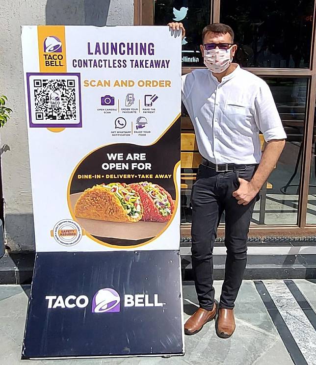 Nitin Karkara, Chief Digital strategist of Taco Bell India, posing in front of Taco Bell which has partnered with DotPe. Photo from DotPe’s Twitter feed.