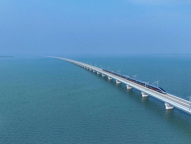 An aerial drone photo shows a train passing through the Yuandang Lake section of the Shanghai-Suzhou-Huzhou high-speed railway on Dec. 26, 2024. A newly constructed high-speed railway began operations on Thursday, enhancing the rail network connecting major cities in east China's Yangtze River Delta Region, a key economic powerhouse of the country. With a designed speed of 350 km per hour and eight stations, the Shanghai-Suzhou-Huzhou high-speed railway spanning 164 km links Shanghai Hongqiao Station with the city of Suzhou City in Jiangsu Province and Huzhou City in Zhejiang Province. (Xinhua/Xing Guangli)