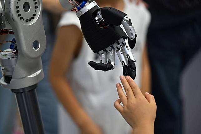 A visitor touches the fingers of a robot at the World Intelligence Expo 2024 in north China's Tianjin, June 22, 2024. (Xinhua/Li Ran)