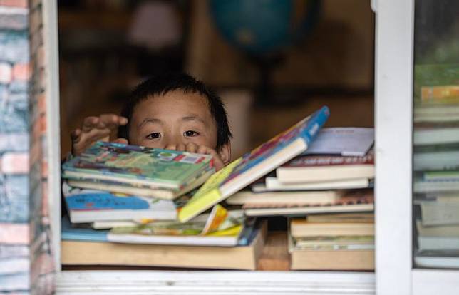A child selects books at the “Banshan Huayu” library in Qiunatong Village in southwest China's Yunnan Province, July 5, 2023. (Xinhua/Fei Maohua)