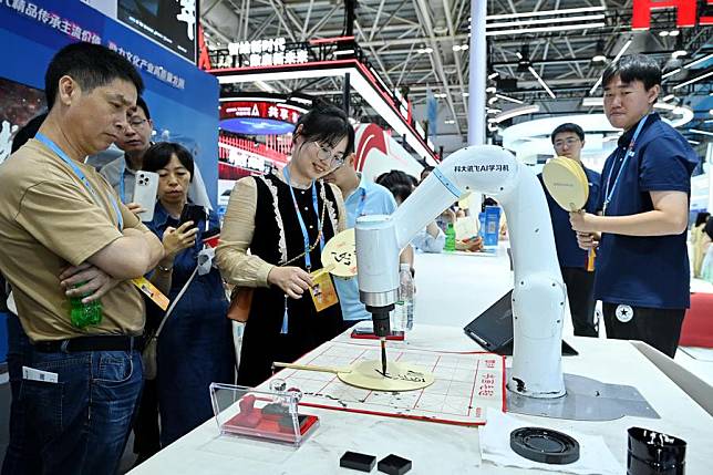 People watch as an AI-powered robotic arm writes with a brush at the hand-on experience area during the 7th Digital China Summit in Fuzhou, southeast China's Fujian Province, May 24, 2024. (Xinhua/Lin Shanchuan)