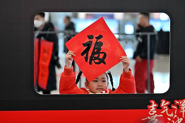 A girl poses for photos with a calligraphy work of Chinese character &ldquo;Fu&rdquo; which means &ldquo;good fortune,&rdquo; at the waiting hall of Taiyuan South Railway Station in Taiyuan, north China's Shanxi Province, Jan. 14, 2025. (Xinhua/Zhan Yan)