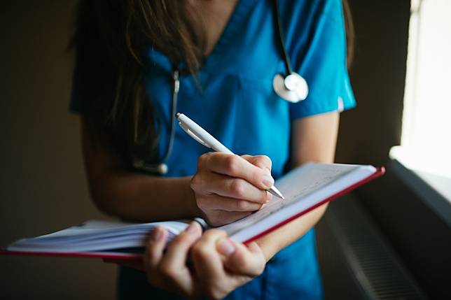 （2021 © Nenad Stojkovic , A nurse writing in a notebook closeup. @ Flickr, CC BY-SA 2.0.）