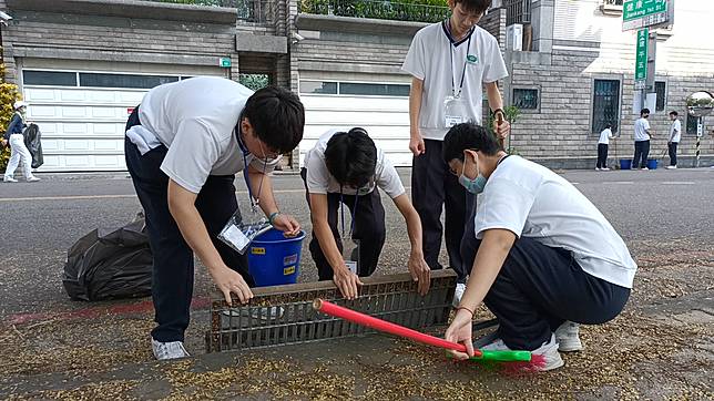 學生們同心協力搬開水溝蓋進行清掃。