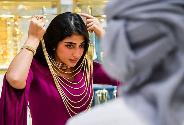 A woman tries on a golden necklace at a stall during the ASJAD Jewelry Exhibition at Alhazm Mall in Doha, Qatar, Oct. 24, 2024. (Photo by Nikku/Xinhua)