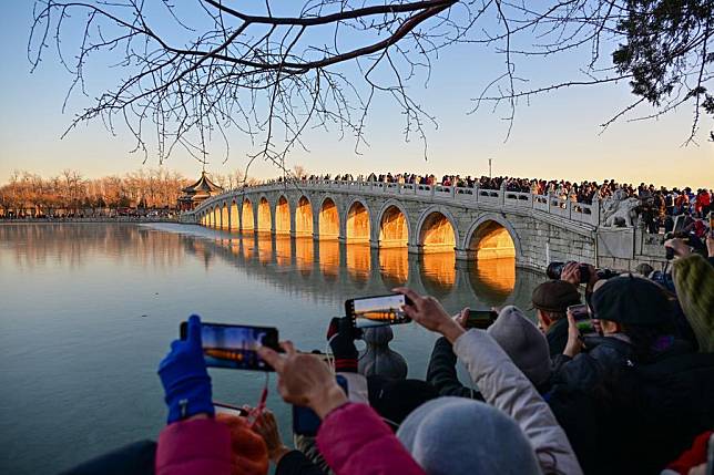 Visitors take photos of the illuminated 17-Arch Bridge at sunset in the Summer Palace in Beijing, capital of China on Dec. 22, 2024. (Xinhua/Li Xin)