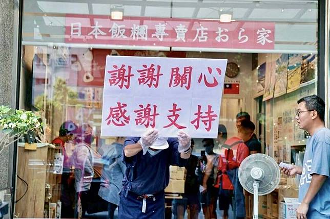 高雄美術館日式飯糰遇到房租高漲、花盆砸店，引發大批市民熱情相挺，老闆舉牌感謝支持。(翻攝臉書)