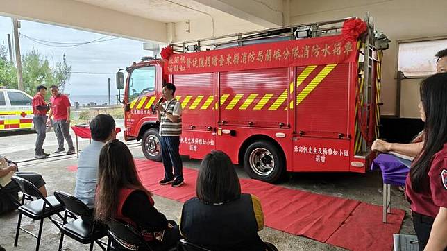 穿著當地傳統服的張詔帆，捐贈小型消防車。(消防局提供)