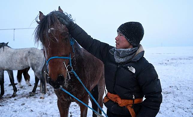 Nairag pats a horse after training in Hulun Buir, north China's Inner Mongolia Autonomous Region, Dec. 15, 2023. (Xinhua/Bei He)